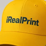 Șapcă galbenă personalizată cu text iRealPrint imprimat în negru – fundal luminos, contrast puternic și vizibilitate maximă pentru branding sau echipe