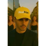 Șapcă galbenă personalizată iRealPrint – model masculin în ținută elegantă, fundal urban cu lumină de apus
