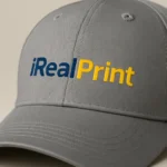 Șapcă gri personalizată cu nume – model iRealPrint cu text imprimat albastru și galben, contrast elegant
