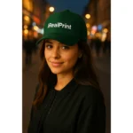 Șapcă verde închis personalizată cu nume iRealPrint – model damă, logo alb imprimat, fundal urban de seară