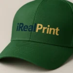 Șapcă verde închis personalizată cu text iRealPrint – logo imprimat albastru și auriu pe fundal verde