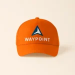 Șapcă portocalie personalizată cu logo companie Waypoint – fundal vibrant, inscripție albă și simbol albastru, accesoriu corporate vizibil și modern