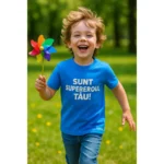 Tricou copii personalizat albastru cu mesaj „Sunt supereroul tău!” – băiețel zâmbitor alergând prin parc, imagine plină de energie și bucurie copilărească