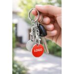 Breloc rosu cu fisa metalica de cumparaturi tinut in mana, obiect promotional vizibil si folosit zilnic pentru memorabilitate crescuta