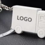 Breloc camion personalizat alb cu ruletă de 1 metru, detaliu logo pe lateral, obiect promoțional pentru firme de transport și logistică