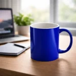 Cană personalizată albastru regal plasată pe birou lângă laptop și agendă într-un cadru office modern, evidențiind contrastul dintre exteriorul albastru intens și interiorul alb al cănii