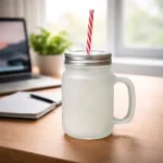 Halbă de limonadă personalizată tip mason jar cu capac metalic și pai, prezentată pe birou într-un cadru modern lângă laptop și agendă