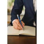 Pix metalic aluminiu personalizat Hello albastru utilizat pentru scrierea notițelor într-un context profesional, pix promoțional metalic cu logo pentru branding corporate și utilizare zilnică în mediul business