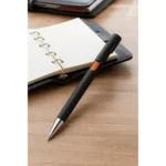 Pix plastic personalizat Nuba Black portocaliu utilizat pentru scriere într-o agendă la birou, produs promoțional corporate pentru branding profesional