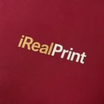 Detaliu logo iRealPrint aplicat prin transfer termic pe tricou damă personalizat roșu Marlboro, evidențiind textura materialului și claritatea personalizării