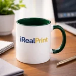 Cană personalizată cu interior verde brad și logo iRealPrint plasată pe birou într-un cadru de lucru modern, sugerând utilizarea zilnică în spații office