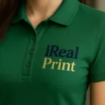 Detaliu personalizare logo iRealPrint aplicat prin transfer termic pe tricou polo damă personalizat verde sticlă, evidențiind textura materialului și claritatea printului