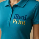 Detaliu personalizare logo iRealPrint aplicat prin transfer termic pe tricou polo damă personalizat turcoaz închis, evidențiind claritatea printului și textura materialului