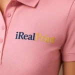 Detaliu personalizare logo iRealPrint aplicat prin transfer termic pe tricou polo damă personalizat roz, evidențiind claritatea printului și textura materialului