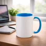 Cană personalizată cu interior albastru ocean plasată pe birou lângă laptop și agendă, sugerând utilizarea zilnică într-un mediu office modern