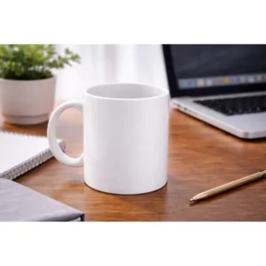 Cană albă personalizată 250ml plasată pe birou lângă laptop, plantă și pix, sugerând utilizarea zilnică într-un mediu office modern