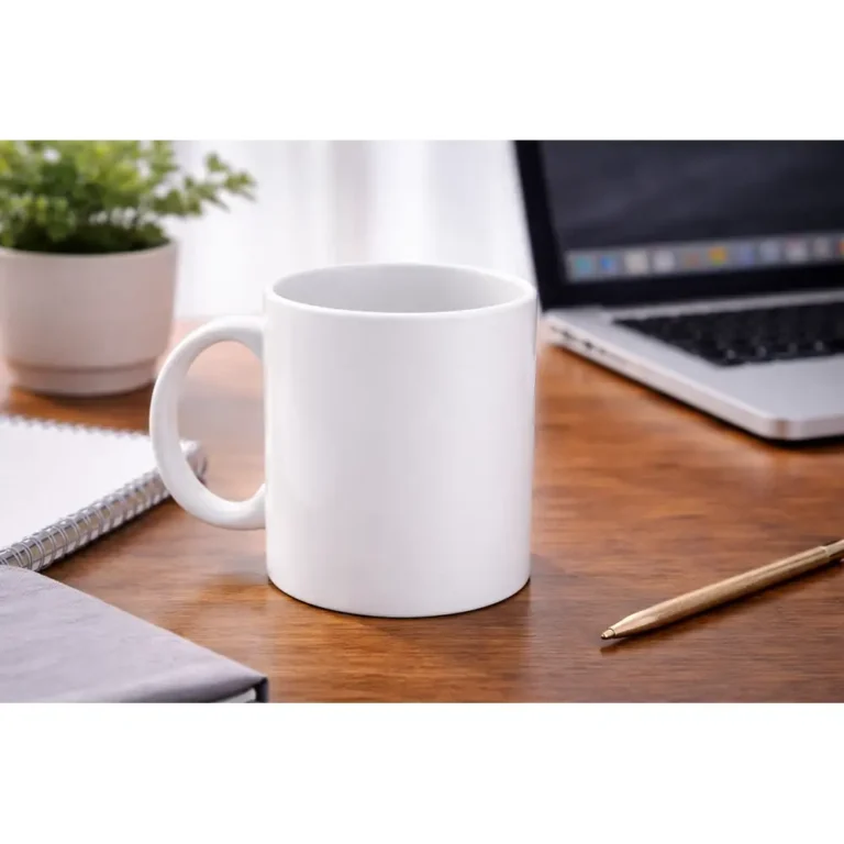 Cană albă personalizată 250ml plasată pe birou lângă laptop, plantă și pix, sugerând utilizarea zilnică într-un mediu office modern