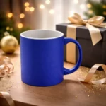 Cană termosensibilă personalizată albastru mat prezentată lângă o cutie cadou elegantă pe fundal festiv, sugerând un cadou original și memorabil