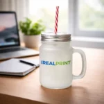 Halbă de limonadă personalizată cu logo iRealPrint plasată pe birou într-un decor luminos de lucru, sugerând utilizarea zilnică pentru băuturi răcoritoare