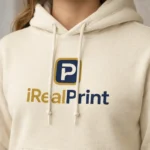 Close-up pe hanorac crem nisip cu logo iRealPrint, evidențiind claritatea și calitatea personalizării prin transfer termic