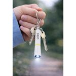Breloc cu lanternă LED galben personalizat folosit la chei, imagine lifestyle cu utilizare reală și lumină activă în exterior