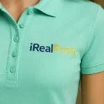 Detaliu personalizare logo iRealPrint aplicat prin transfer termic pe tricou polo damă personalizat verde mentă, evidențiind claritatea printului și textura materialului