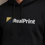 Prim-plan hanorac personalizat bărbați negru cu logo iRealPrint aplicat prin transfer termic, evidențiind claritatea personalizării și textura materialului