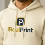 Detaliu hanorac bărbați crem nisip cu logo iRealPrint aplicat prin transfer termic profesional, evidențiind claritatea printului, contrastul elegant și calitatea personalizării premium
