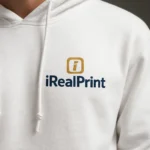 Detaliu hanorac bărbați alb personalizat cu logo iRealPrint aplicat prin transfer termic premium, evidențiind claritatea graficii și contrastul elegant dintre personalizare și materialul alb al hanoracului