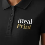Detaliu logo iRealPrint aplicat prin transfer termic pe tricou polo damă gri antracit, contrast clar pe material premium