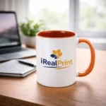 Cană personalizată cu interior portocaliu și logo iRealPrint pe birou într-un cadru luminos, evidențiind contrastul vizual și impactul personalizării