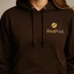 Close-up pe hanorac ciocolată dark cu logo iRealPrint, accent pe claritatea și contrastul personalizării