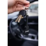 Breloc desfăcător de sticle chitară negru folosit pe chei auto în context real, accesoriu promoțional metalic pentru utilizare zilnică și expunere constantă a logo-ului