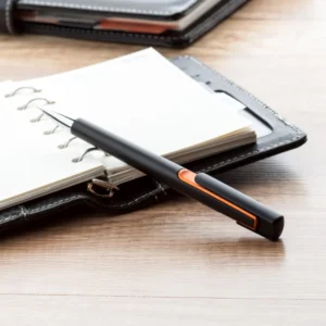 Pix plastic personalizat Nuba Black portocaliu așezat lângă agendă în context business, produs promoțional utilizat în birouri și întâlniri profesionale