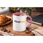 Cană personalizată cu interior roz pastel și logo iRealPrint într-un decor lifestyle cu boabe de cafea și accesorii elegante, sugerând un moment relaxant de cafea