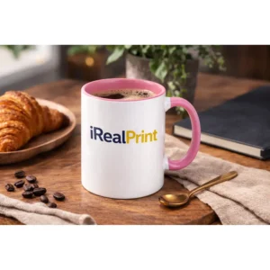 Cană personalizată cu interior roz pastel și logo iRealPrint într-un decor lifestyle cu boabe de cafea și accesorii elegante, sugerând un moment relaxant de cafea