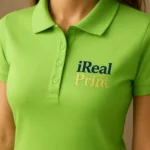 Detaliu personalizare logo iRealPrint aplicat prin transfer termic pe tricou polo damă personalizat verde iarbă, evidențiind claritatea printului