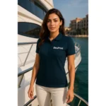 Model feminin purtând tricou polo damă personalizat albastru navy într-un cadru premium lângă yacht, ilustrând utilizarea pentru branding profesional și uniforme corporate