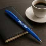 Pix bambus personalizat Foxy albastru navy așezat pe o agendă lângă o ceașcă de cafea, obiect promoțional eco utilizat în mediul business