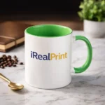 Cană personalizată cu interior verde lime și logo iRealPrint într-un decor lifestyle cu boabe de cafea și obiecte elegante, sugerând un moment relaxant de cafea