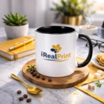Cană personalizată cu interior negru onyx și logo iRealPrint prezentată într-un decor elegant cu linguriță aurie și elemente premium de cafea