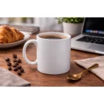 Cană albă personalizată 250ml cu băutură caldă pe birou lângă laptop, croissant și accesorii office, evidențiind utilizarea practică în rutina zilnică de lucru