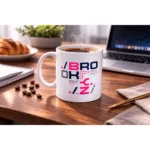 Cană albă personalizată 350ml cu cafea fierbinte pe birou lângă croissant și accesorii office, sugerând rutina de dimineață la birou