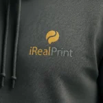 Detaliu hanorac bărbați charcoal cu logo iRealPrint în nuanță gold aplicat prin transfer termic profesional, evidențiind claritatea designului, textura materialului premium și contrastul elegant al personalizării
