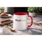 Cană personalizată cu interior roșu cherry și logo iRealPrint într-un decor elegant cu linguriță aurie și elemente premium, sugerând un moment rafinat de cafea
