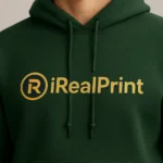 Detaliu hanorac personalizat verde forest cu logo iRealPrint auriu pe piept, evidențiind contrastul elegant și designul premium