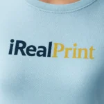 Detaliu logo iRealPrint aplicat prin transfer termic pe tricou damă personalizat albastru deschis, personalizare clară și contrast vizibil