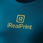 Detaliu personalizare logo iRealPrint pe tricou unisex albastru petrol, transfer termic clar pe material textil premium