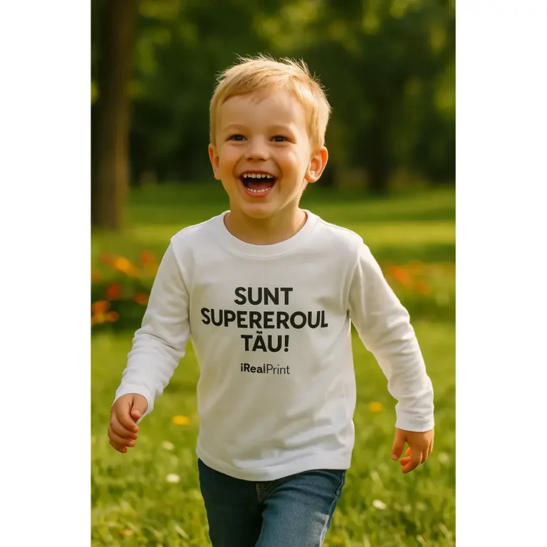 Copil purtând bluză albă personalizată cu mesaj Sunt Supereroul Tău în timpul jocului în parc