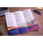 Pliant DL personalizat deschis pe birou lângă laptop, exemplu real de utilizare pentru promovare profesională și distribuție eficientă